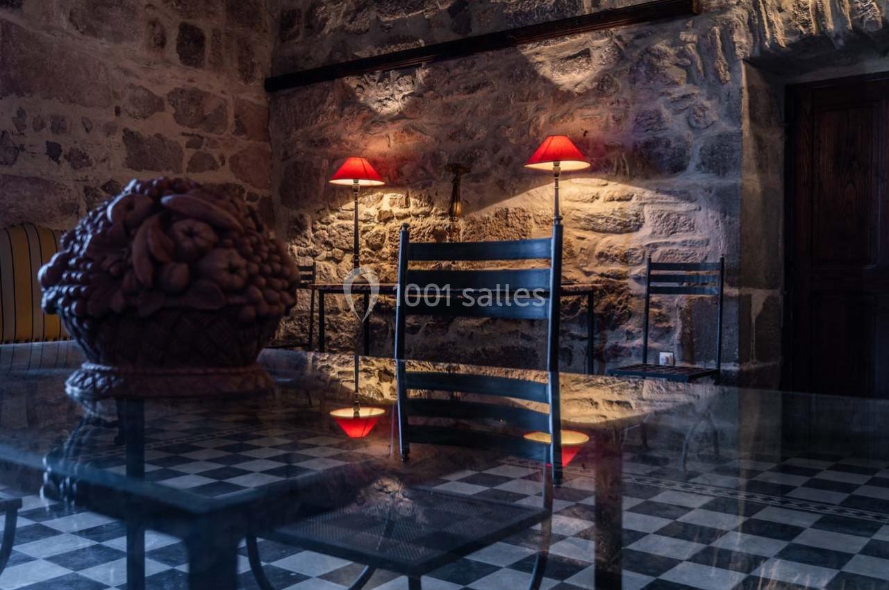 Salle en pierre avec éclairage tamisé, table en verre réfléchissant un panier décoratif et des chaises en métal.