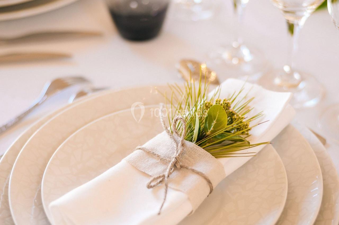 Serviette blanche pliée avec un brin de verdure et une ficelle, posée sur une assiette dans une table élégamment dressée.