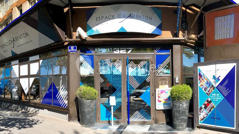 Façade vitrée de l'Espace Charenton avec des affiches et des décorations géométriques bleues et blanches.