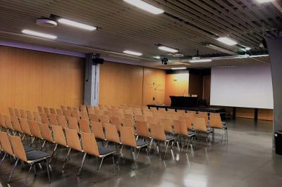 Salle de réunion avec tables disposées en U, bouteilles d'eau et gobelets, panneau d'information en arrière-plan.