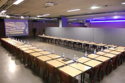 Salle de réunion avec tables disposées en U, bouteilles d'eau et gobelets, panneau d'information en arrière-plan.