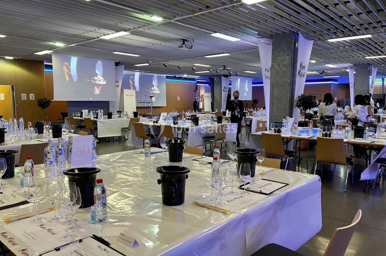 Salle de dégustation aménagée avec des tables dressées, verres, crachoirs et documents, prête pour un événement.