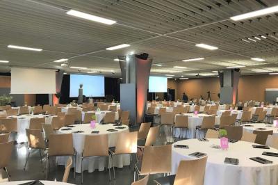Salle de réunion avec tables disposées en U, bouteilles d'eau et gobelets, panneau d'information en arrière-plan.