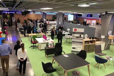 Salle de réunion avec tables disposées en U, bouteilles d'eau et gobelets, panneau d'information en arrière-plan.