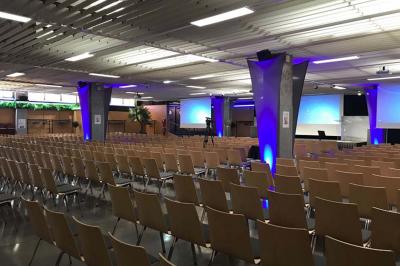 Salle de réunion avec tables disposées en U, bouteilles d'eau et gobelets, panneau d'information en arrière-plan.