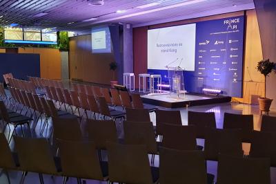 Salle de réunion avec tables disposées en U, bouteilles d'eau et gobelets, panneau d'information en arrière-plan.