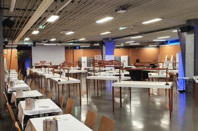 Salle de réunion avec tables disposées en U, bouteilles d'eau et gobelets, panneau d'information en arrière-plan.