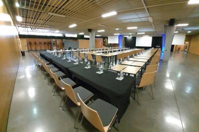 Salle de réunion avec tables disposées en U, bouteilles d'eau et gobelets, panneau d'information en arrière-plan.