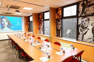 Salle de réunion avec tables disposées en U, bouteilles d'eau et gobelets, panneau d'information en arrière-plan.
