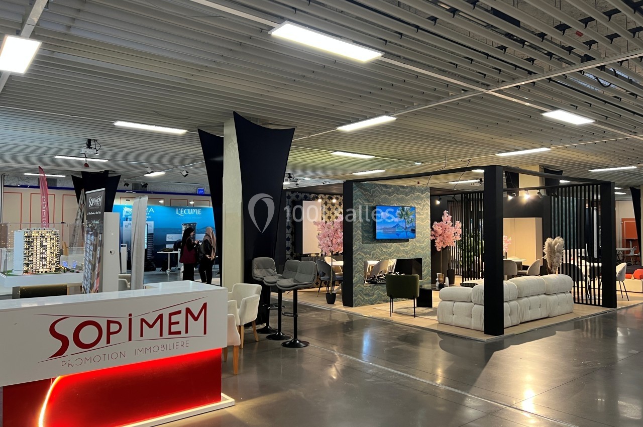 Vue d'un espace d'exposition avec stands aménagés, mobilier moderne et éclairage intérieur.