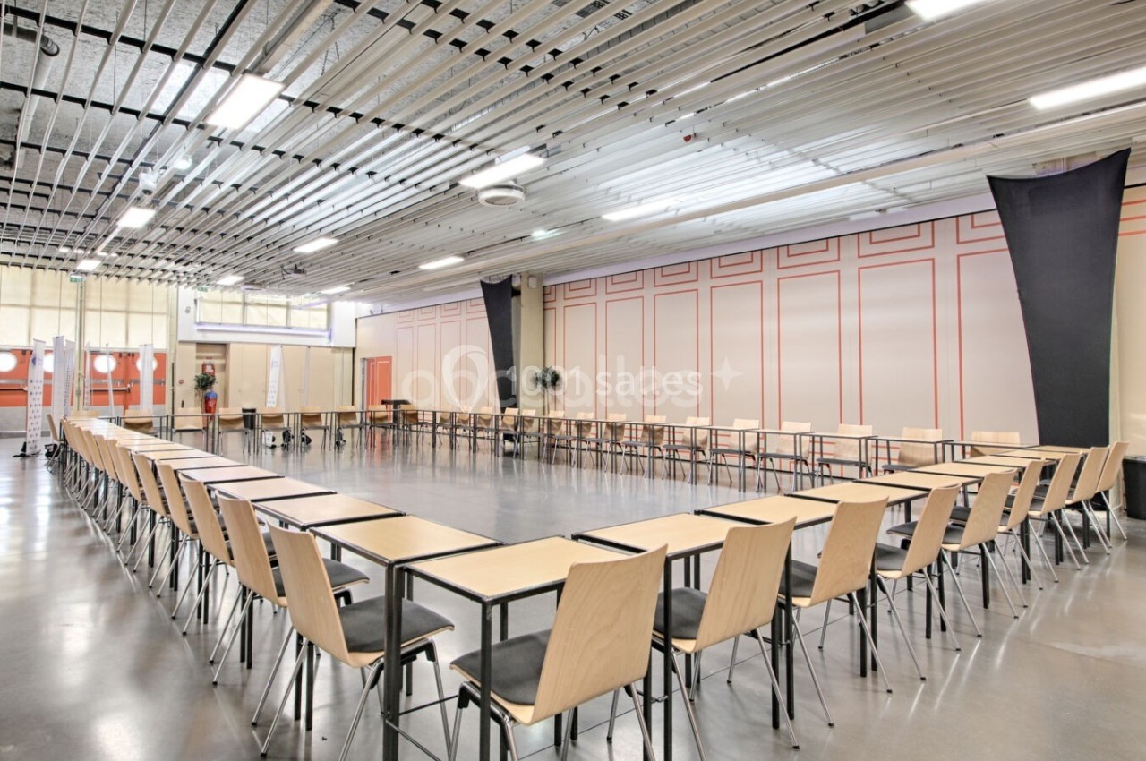 Salle de réunion lumineuse avec des tables et chaises disposées en U, entourée de murs clairs et d'un plafond industriel.