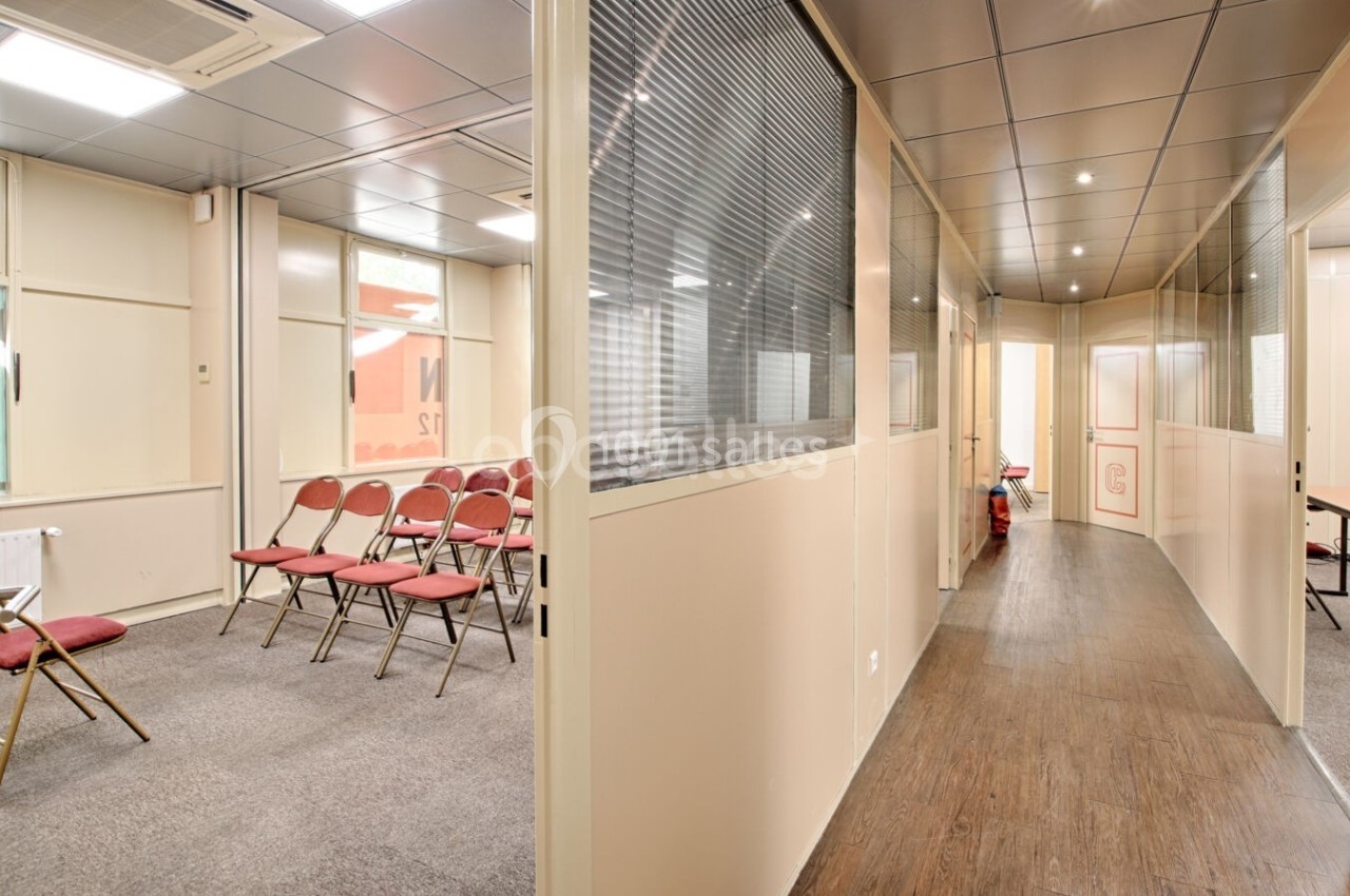 Salle de réunion avec chaises rouges alignées, couloir adjacent et cloisons vitrées dans un espace professionnel.