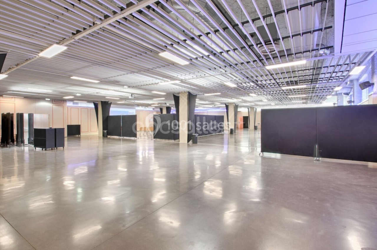 Espace intérieur vaste et lumineux avec sol en béton poli, colonnes et plafond métallique structuré.