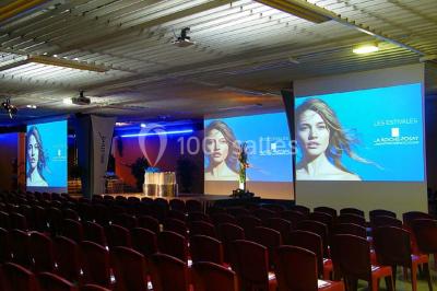 Salle de réunion avec tables disposées en U, bouteilles d'eau et gobelets, panneau d'information en arrière-plan.