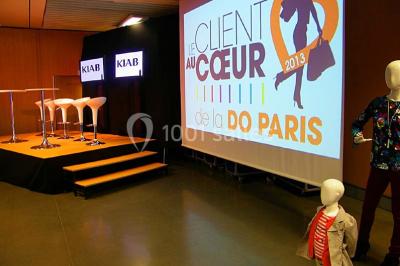 Salle de réunion avec tables disposées en U, bouteilles d'eau et gobelets, panneau d'information en arrière-plan.