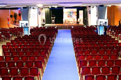 Salle de réunion avec tables disposées en U, bouteilles d'eau et gobelets, panneau d'information en arrière-plan.
