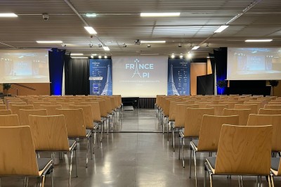 Salle de réunion avec tables disposées en U, bouteilles d'eau et gobelets, panneau d'information en arrière-plan.