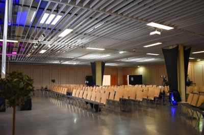 Salle de réunion avec tables disposées en U, bouteilles d'eau et gobelets, panneau d'information en arrière-plan.