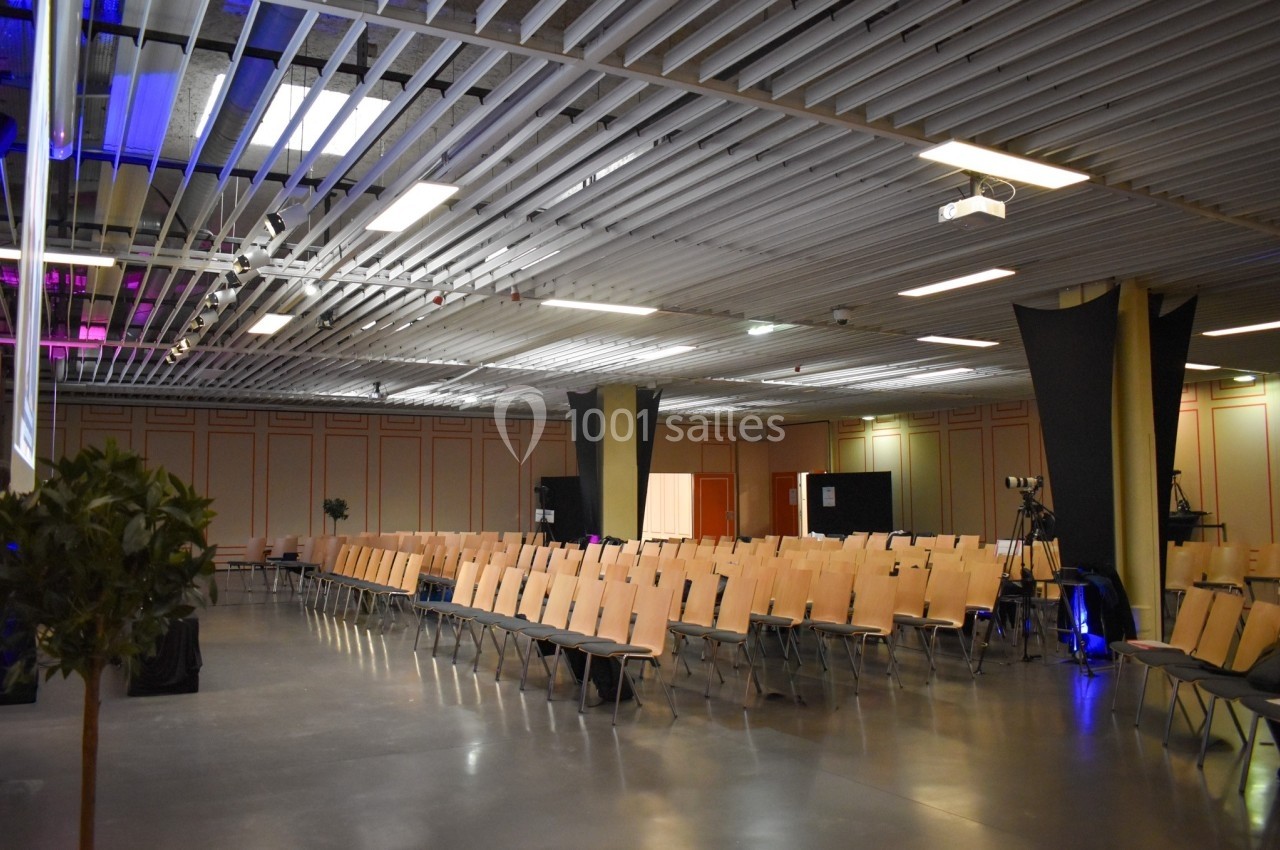 Salle de conférence vide avec des rangées de chaises alignées et un éclairage tamisé.