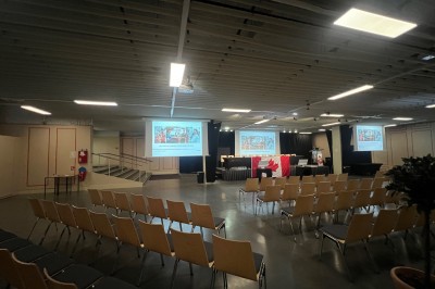 Salle de réunion avec tables disposées en U, bouteilles d'eau et gobelets, panneau d'information en arrière-plan.