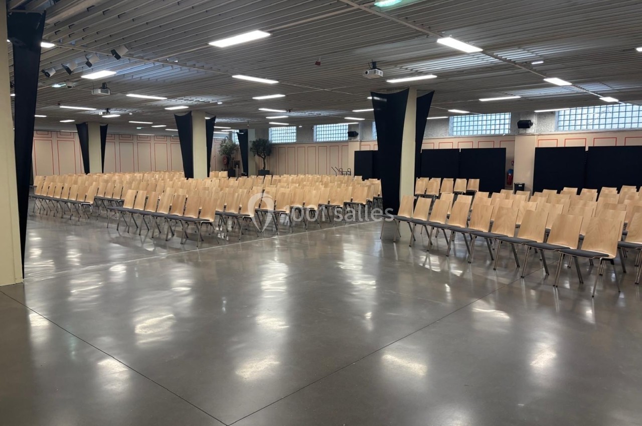 Salle de conférence vide avec rangées de chaises en bois alignées sur un sol en béton poli.