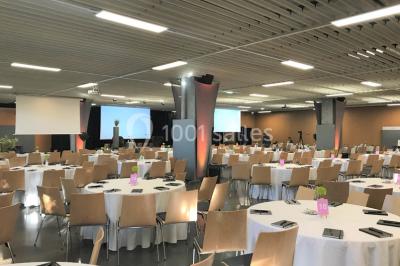 Salle de réunion avec tables disposées en U, bouteilles d'eau et gobelets, panneau d'information en arrière-plan.