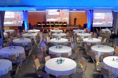Salle de réunion avec tables disposées en U, bouteilles d'eau et gobelets, panneau d'information en arrière-plan.