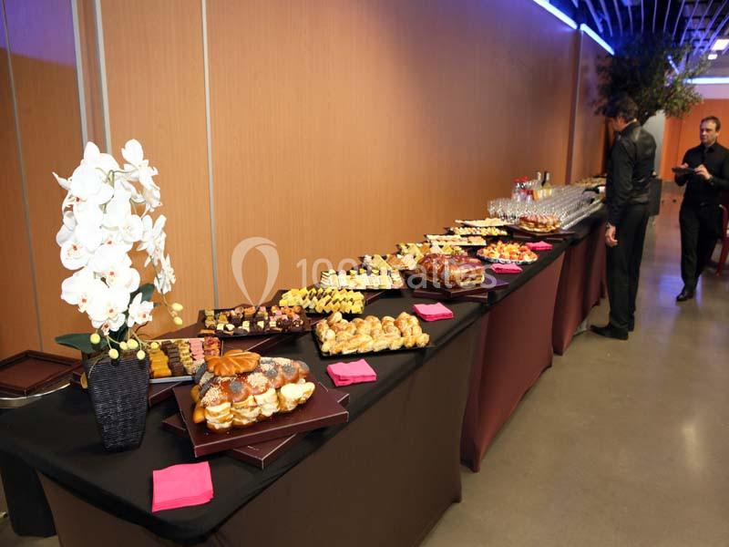 Buffet composé de pâtisseries, viennoiseries et desserts variés, disposés sur une longue table avec une orchidée blanche.