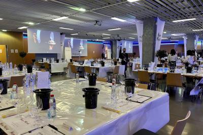 Salle de réunion avec tables disposées en U, bouteilles d'eau et gobelets, panneau d'information en arrière-plan.