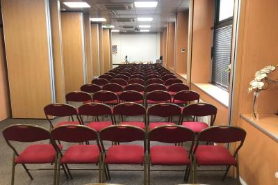 Salle de réunion avec tables disposées en U, bouteilles d'eau et gobelets, panneau d'information en arrière-plan.
