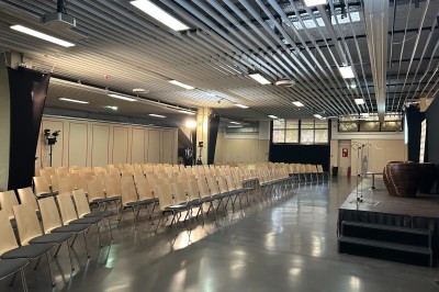 Salle de réunion avec tables disposées en U, bouteilles d'eau et gobelets, panneau d'information en arrière-plan.