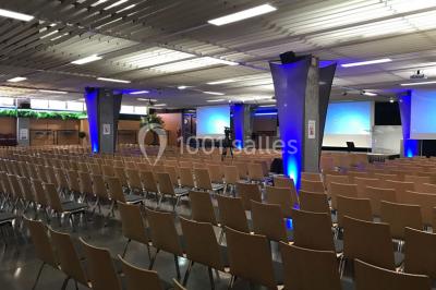 Salle de réunion avec tables disposées en U, bouteilles d'eau et gobelets, panneau d'information en arrière-plan.