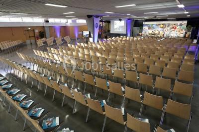 Salle de réunion avec tables disposées en U, bouteilles d'eau et gobelets, panneau d'information en arrière-plan.