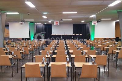 Salle de réunion avec tables disposées en U, bouteilles d'eau et gobelets, panneau d'information en arrière-plan.