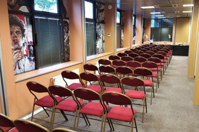 Salle de réunion avec tables disposées en U, bouteilles d'eau et gobelets, panneau d'information en arrière-plan.