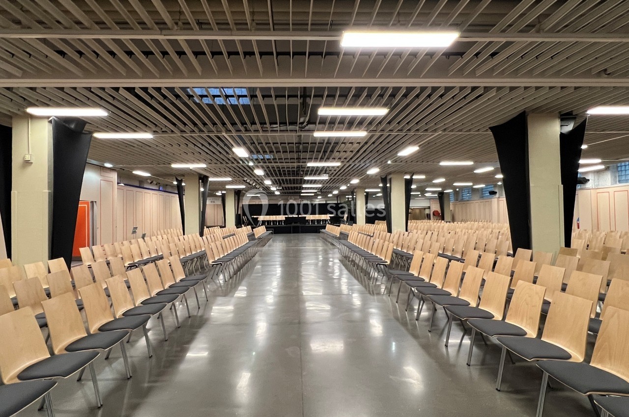 Salle de conférence vide avec des rangées de chaises en bois alignées de part et d'autre d'une allée centrale.