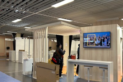 Salle de réunion avec tables disposées en U, bouteilles d'eau et gobelets, panneau d'information en arrière-plan.
