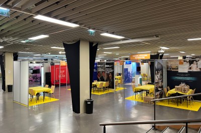 Salle de réunion avec tables disposées en U, bouteilles d'eau et gobelets, panneau d'information en arrière-plan.