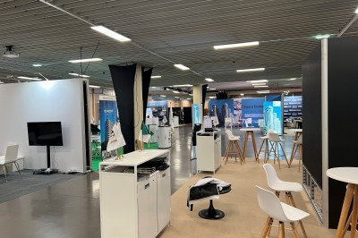 Salle de réunion avec tables disposées en U, bouteilles d'eau et gobelets, panneau d'information en arrière-plan.
