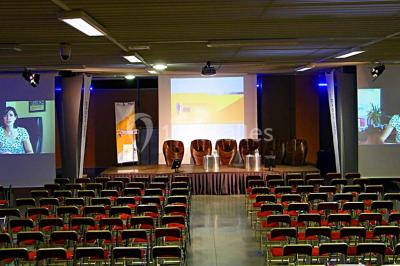 Salle de réunion avec tables disposées en U, bouteilles d'eau et gobelets, panneau d'information en arrière-plan.