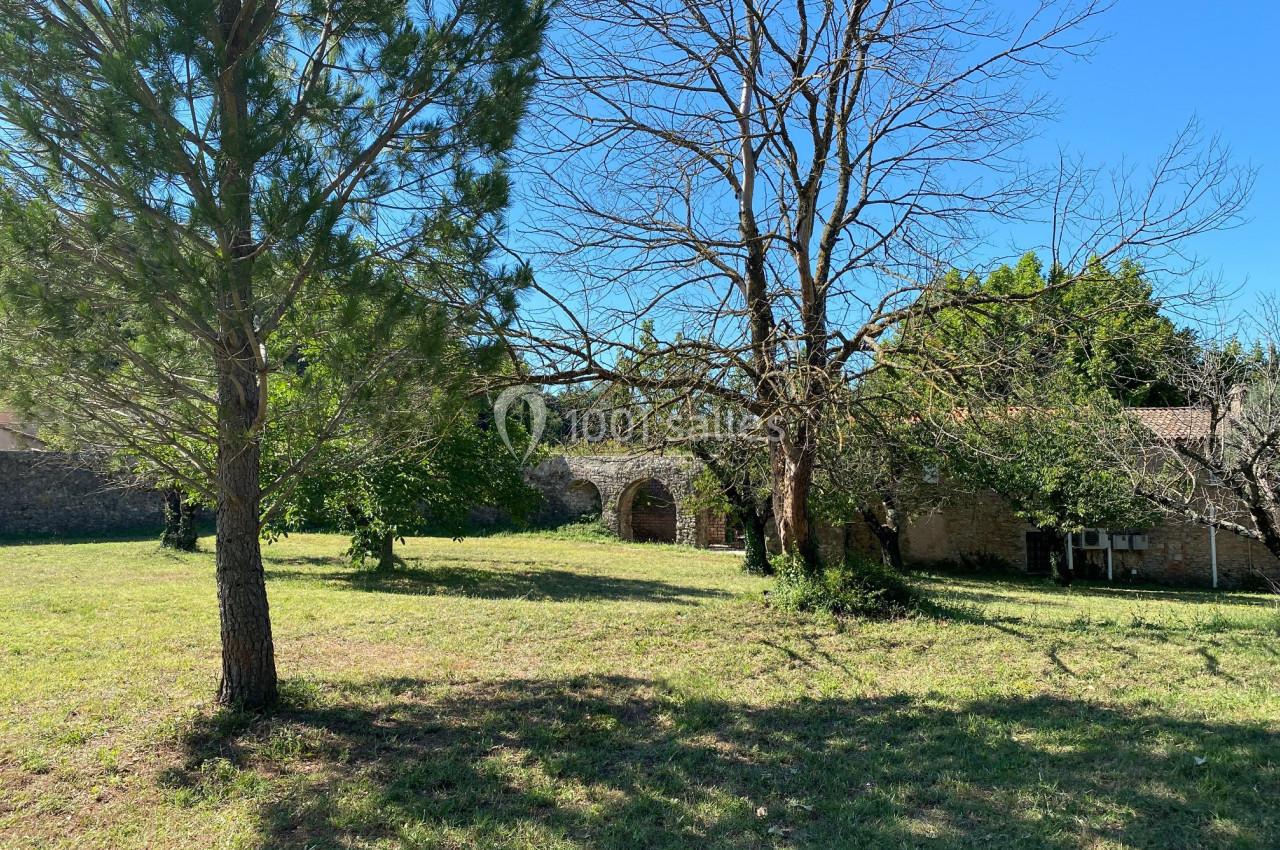 Jardin verdoyant avec arbres, herbe et bâtiments en pierre sous un ciel bleu clair.