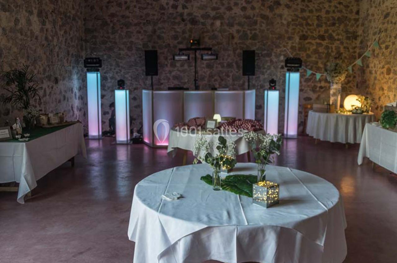 Salle en pierre aménagée pour un événement, avec tables décorées et un espace DJ éclairé.