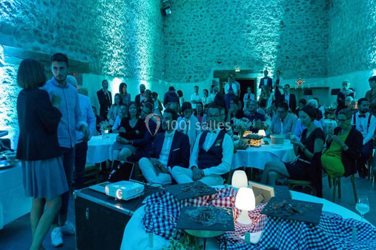 Des invités assis et debout dans une salle en pierre éclairée de lumières bleues, lors d'un événement festif.