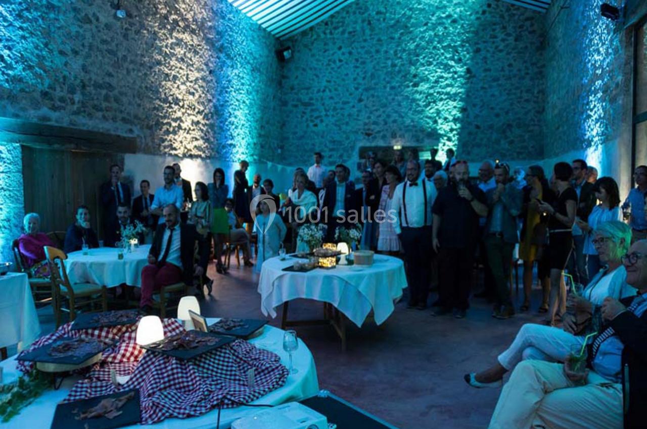 Groupe de personnes rassemblées dans une salle en pierre éclairée par des lumières bleues, avec des tables décorées.
