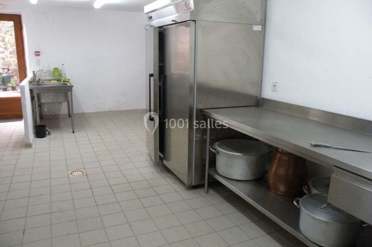 Cuisine professionnelle avec sol carrelé, plan de travail en inox, réfrigérateur et évier en arrière-plan.