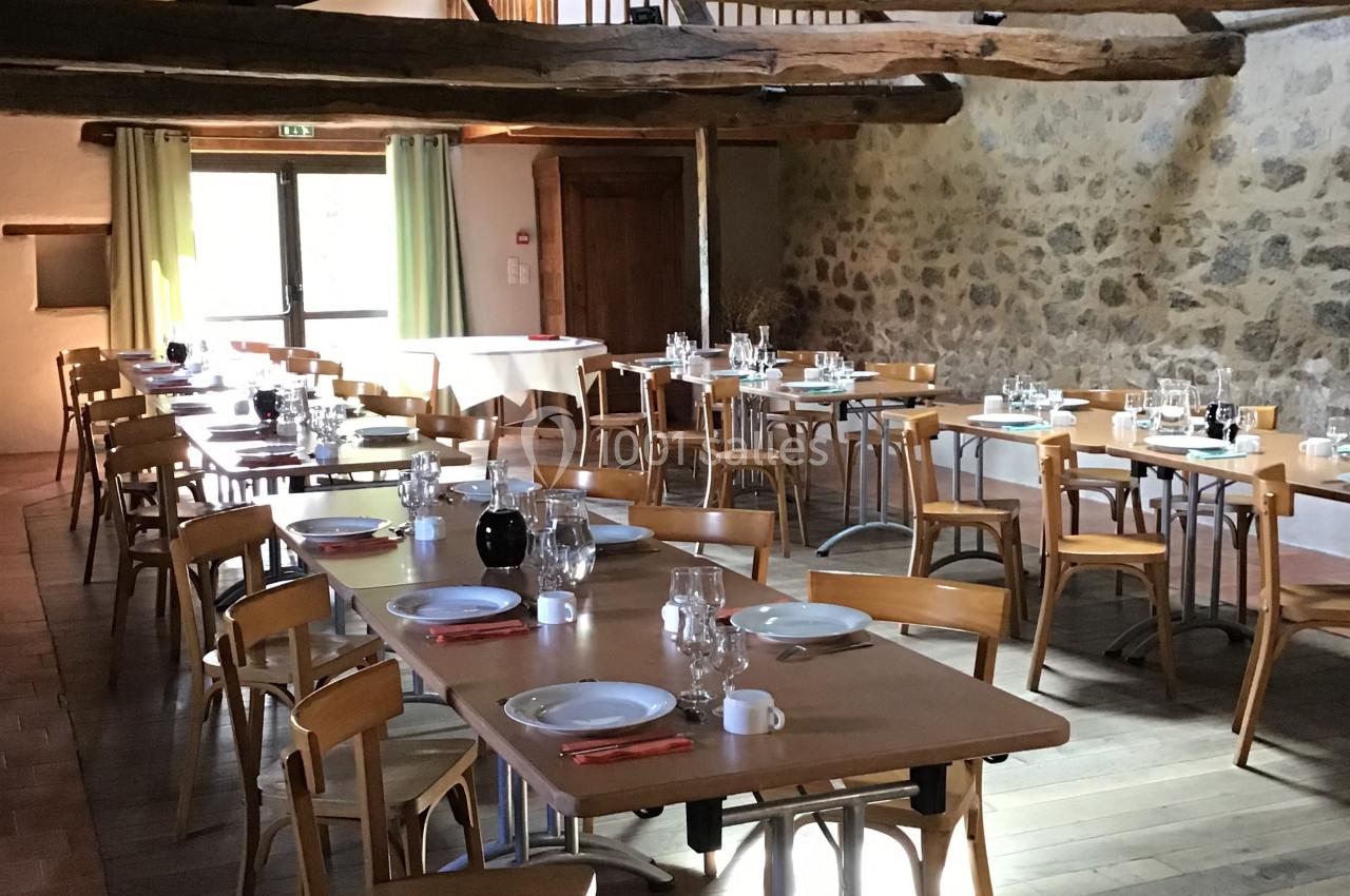 Salle à manger lumineuse avec tables en bois dressées, poutres apparentes et murs en pierre.
