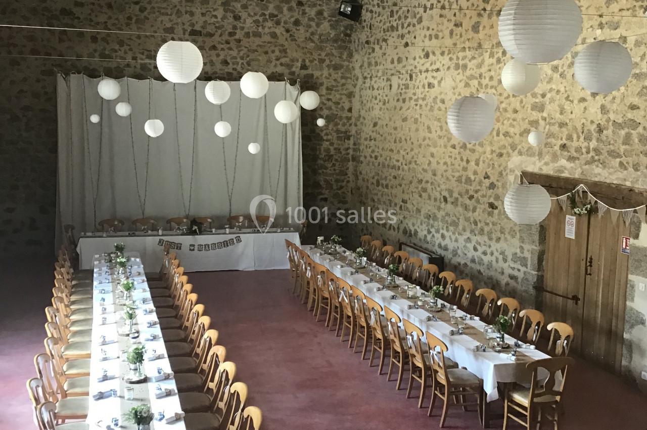 Salle en pierre avec deux longues tables dressées pour un repas, décorée de lanternes suspendues et d'éléments naturels.