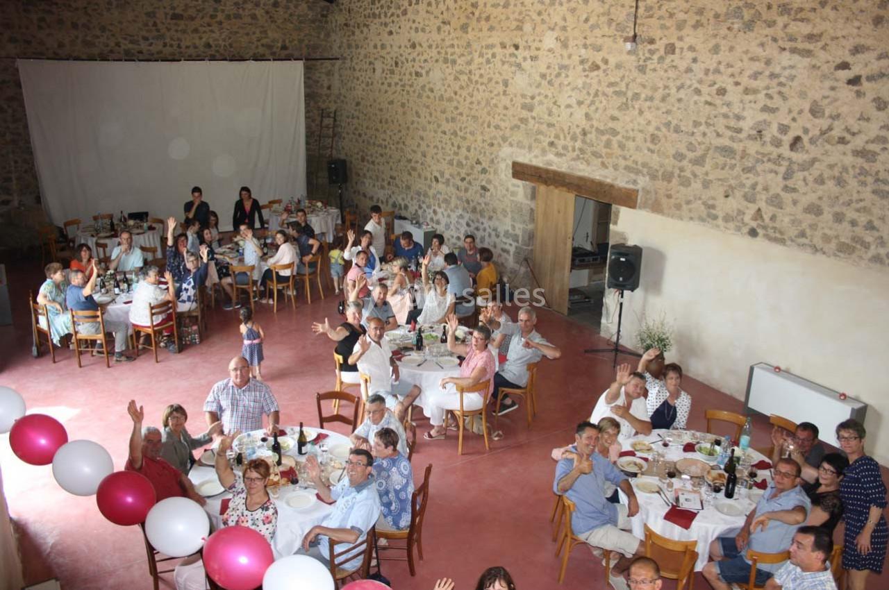 Des convives assis à des tables rondes dans une grande salle en pierre, participant à un événement festif.