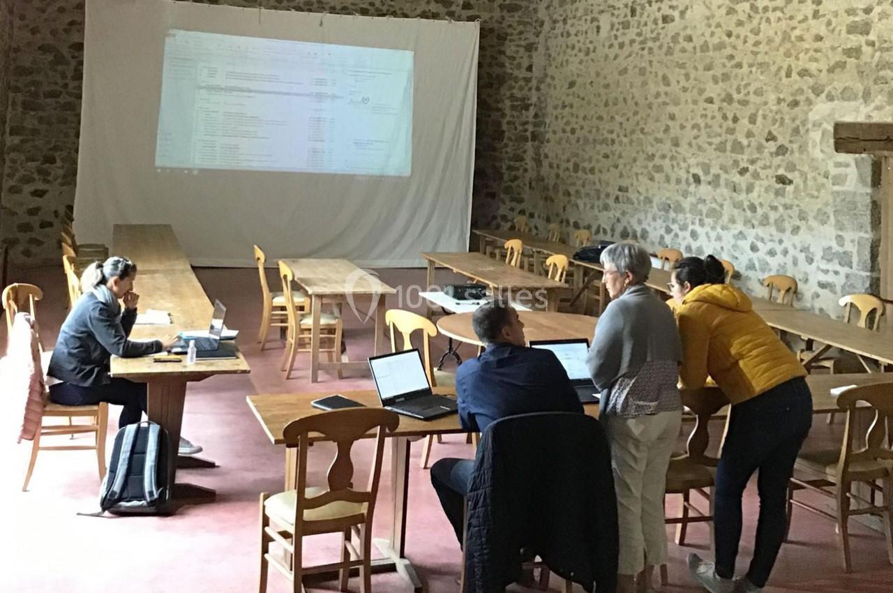 Des personnes travaillent en groupe dans une salle en pierre avec des tables, des chaises et un écran de projection.