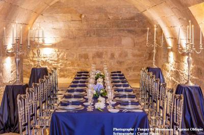 Salle lumineuse avec parquet en bois, table ronde dressée avec nappe rouge, et moulures décoratives au plafond.